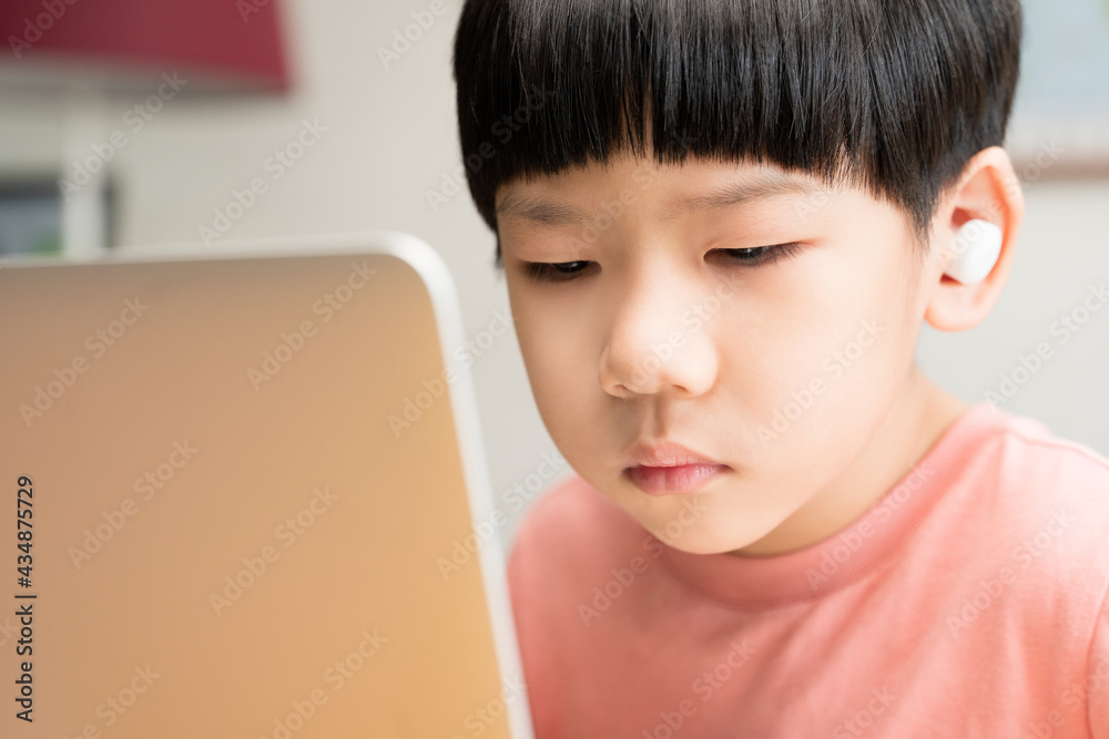 Kids mental health during Covid-19 pandemic concept. Portrait of a smart asian student boy with wireless earbuds using tablet computer to join online classroom from home. New normal, Fatigue, Tired. Kids mental health during Covid-19 pandemic concept. Portrait of a smart asian student boy with wireless earbuds using tablet computer to join online classroom from home. New normal, Fatigue, Tired.