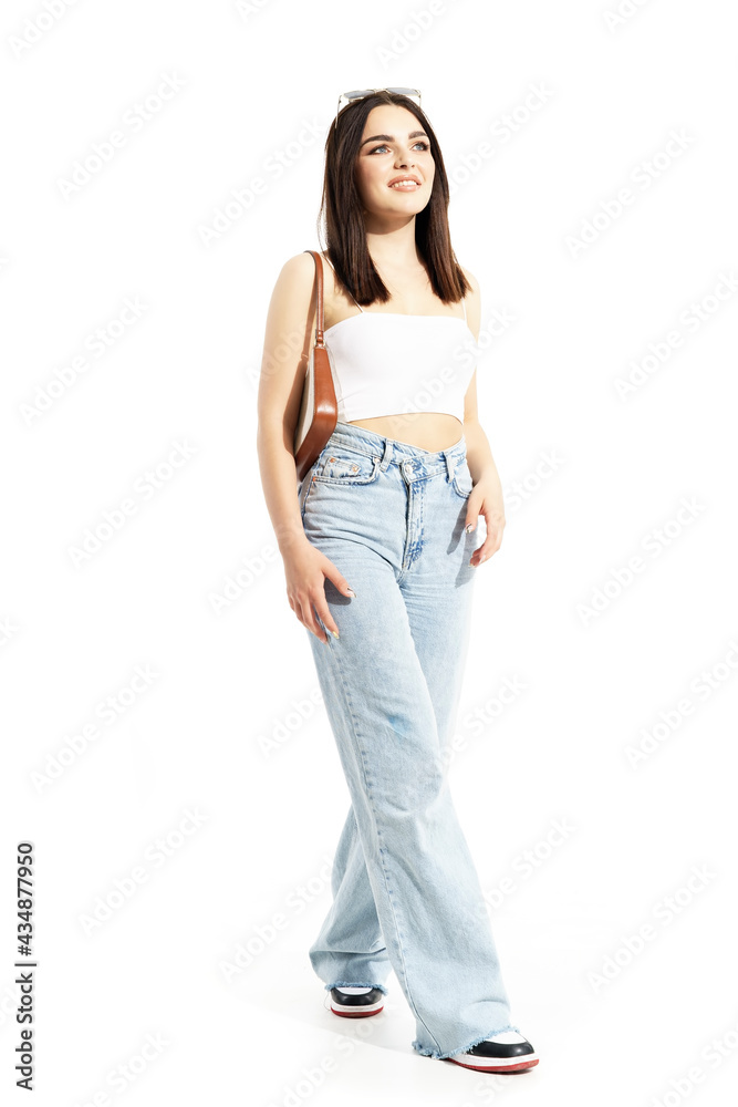 Happy beautiful young trendy gen Z woman with hand bag walking and watching up. Full body length isolated on white background Happy beautiful young trendy gen Z woman with hand bag walking and watching up. Full body length isolated on white background
