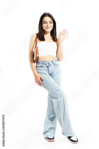 Summer style girl with attitude greeting and waving hand pretending to smile. Full body length isolated on white background