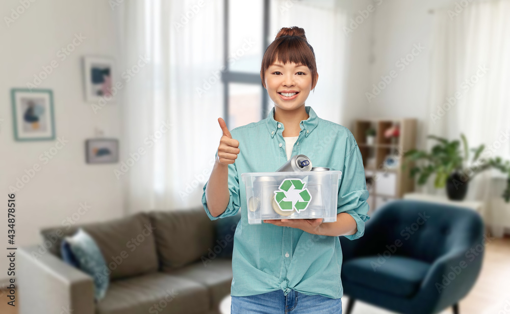 metal recycling, waste sorting and sustainability concept - smiling young asian woman holding plastic box with tin cans showing thumbs up over home living room background metal recycling, waste sorting and sustainability concept - smiling young asian woman holding plastic box with tin cans showing thumbs up over home living room background