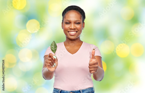eco living, environment and sustainability concept - portrait of happy smiling young african american woman holding leaf over lights on green background