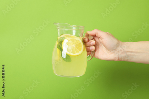 Female hand holds jug with lemonade on green background