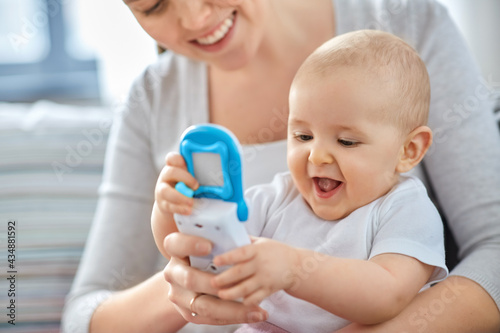 family, motherhood and people concept - happy smiling mother and little baby playing with toy phone at home photo