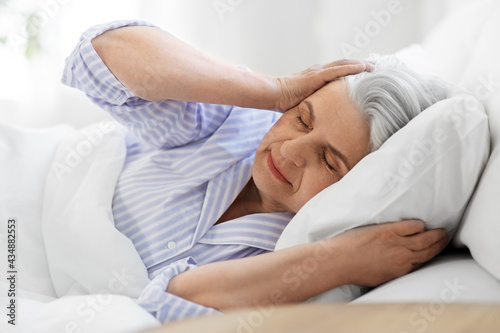 bedtime, rest and old people concept - annoyed senior woman in pajamas suffering from headache lying in bed at home bedroom