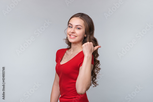 Portrait of cheerful young brunette woman, pointing aside thumb and smiling, inviting people look promo