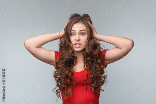 Portrait of young brunette woman in panic grabbing her head in fear or frustration. Studio shot, gray background