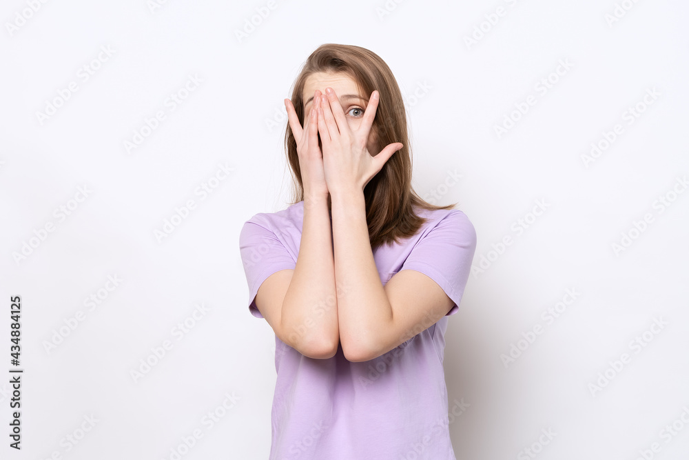 scared girl hiding face in palms hands and peering out with one eye between her fingers, trembling fear scared girl hiding face in palms hands and peering out with one eye between her fingers, trembling fear