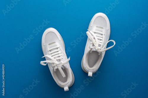 White sports sneakers isolated on a blue background, doing sports and training in the hall, healthy lifestyle, top view, copy space