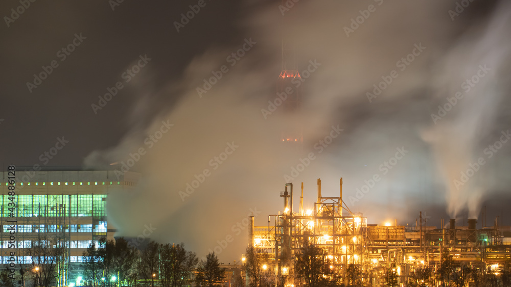 View of a large factory or plant in the light of night lighting. A lot of smoke comes out of the factory's chimneys. Pollution of the environment. fire at a waste recycling plant