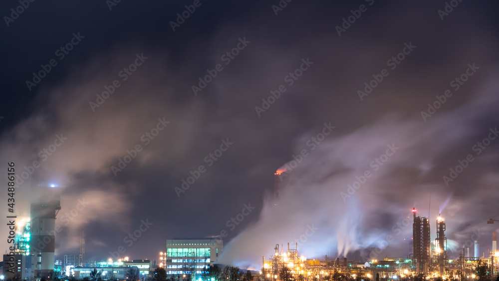 View of a large factory or plant in the light of night lighting. A lot of smoke comes out of the factory's chimneys. Pollution of the environment. Toxic bad ecology