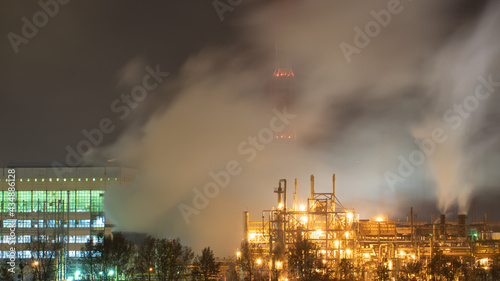View of a large factory or plant in the light of night lighting. A lot of smoke comes out of the factory s chimneys. Pollution of the environment. fire at a waste recycling plant