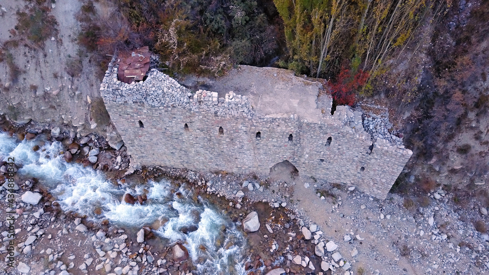 Naklejka premium The stone castle on the banks of the river. View of the stone fortress from a drone, from a height. A mountain river runs, large stones lie on the Bank. Yellow-red trees of the forest, autumn has come