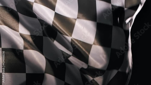 Racing flag silk fabric fluttering wave on black studio background. Checkered flag formula one car motor sport. Official finish start race. Racing flag waving. Slow motion. Close up. photo