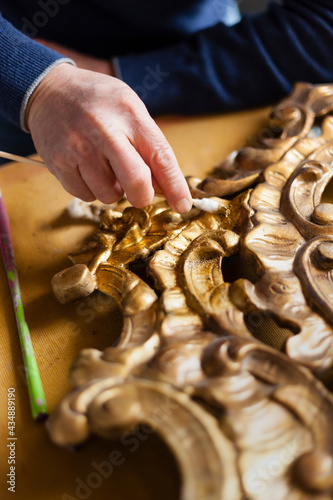 Classic art and antiques restoration concept with a golden leaf frame being cleaned by a man hands using cotton with delicacy.