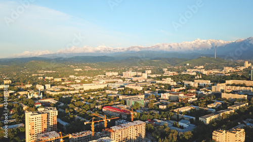 Bright color sunset over the city of Almaty. Huge clouds over the mountains and the city shimmer from bright blue to yellow and dark blue. Tall houses and green trees  cars driving on the roads.