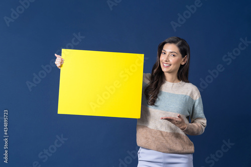 Happy young smiling Asian woman holding and presenting to copy space empty yellow billboard on blue color background, thinking and specking via balloon blank paper, advertisement Concept