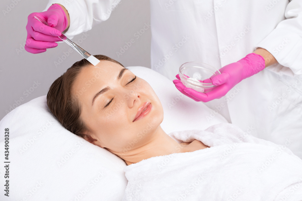 © Dimid - Beautician makes a face mask of a woman to rejuvenate the skin. Cosmetology treatment of problem skin on the face and body.