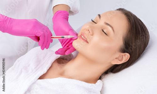 Cosmetologist does injections for lips augmentation and anti wrinkle in the nasolabial folds of a beautiful woman. Women's cosmetology in the beauty salon.