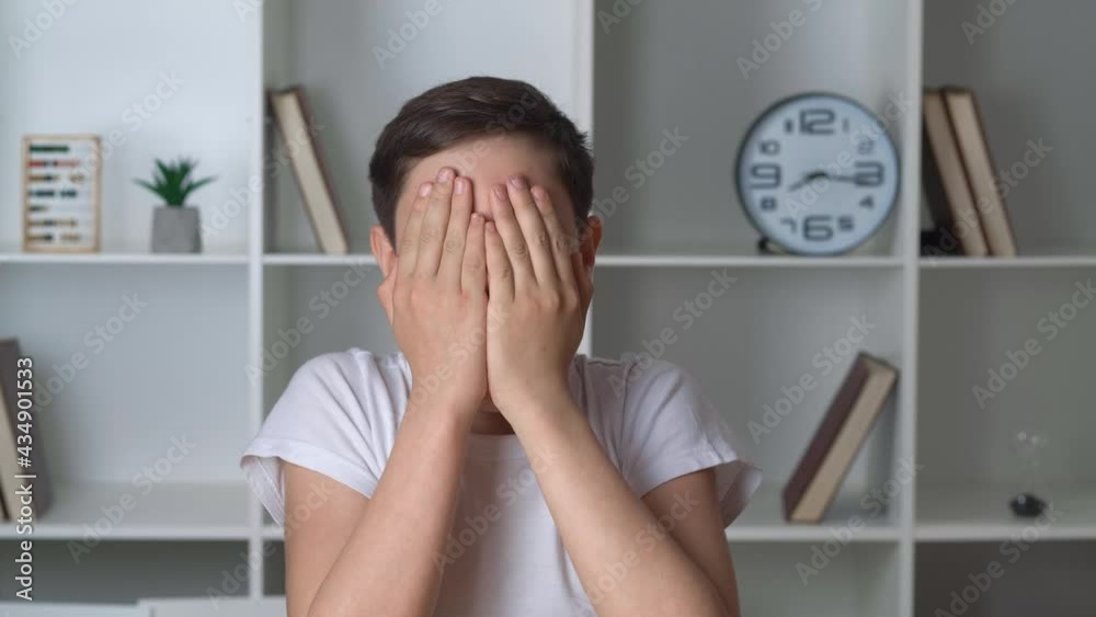 Portrait of a frightened child, sees the terrible and covers his face with his hands in horror. Boy watching a horror movie and gets scared while sitting at home