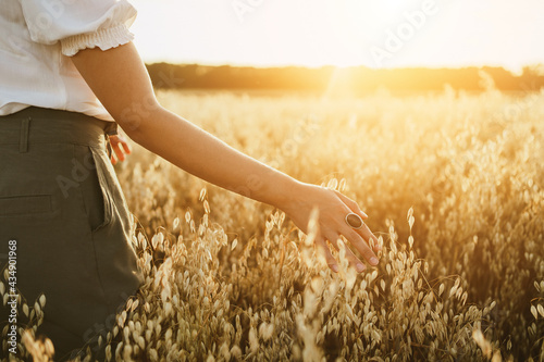 Young woman in a oats field. Girl walking through field and touches cereal. Rich Harvest concept. Banner with copy space.