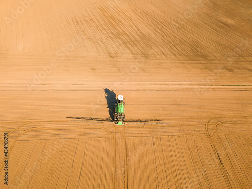 View from a drone on a tractor, spraying fertilizers, chemicals, soil in the spring in the field