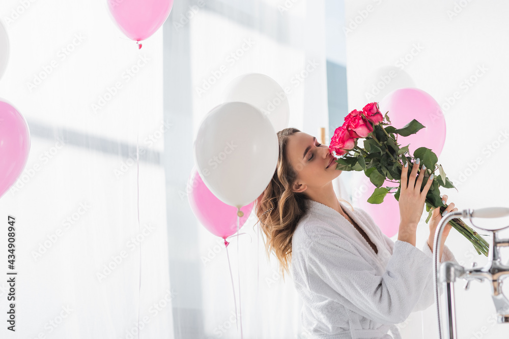 Young woman in bathrobe smelling roses near balloons in bathroom - obrazy, fototapety, plakaty 