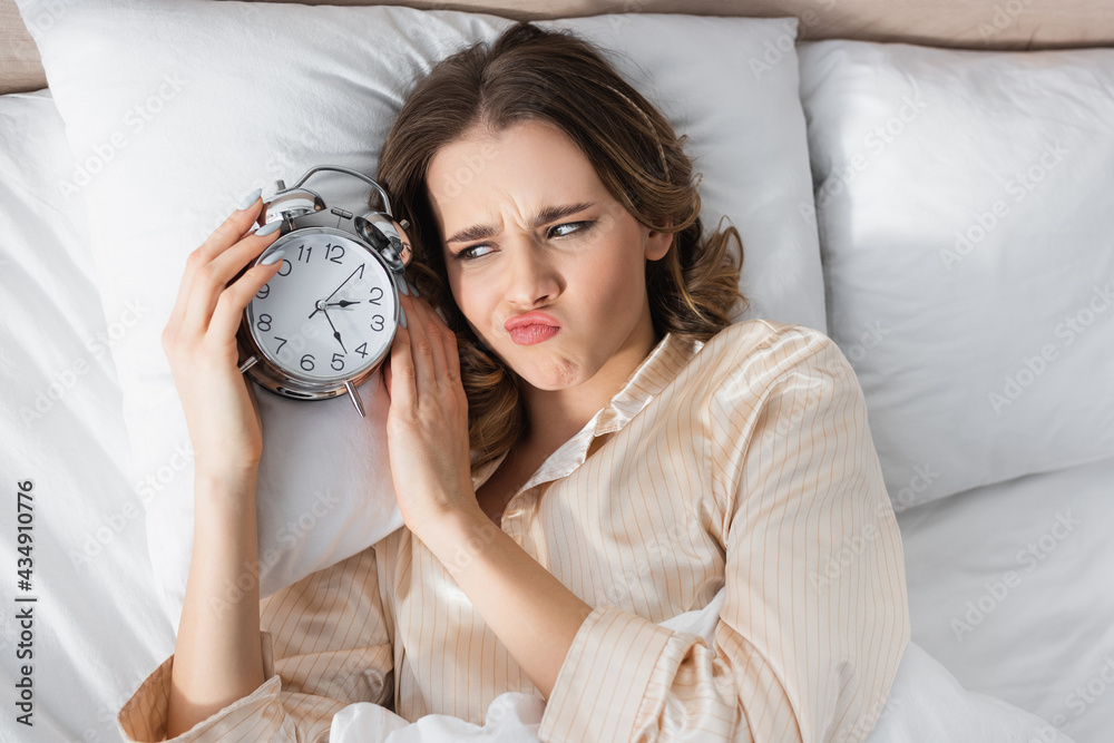 Top view of upset woman looking at alarm clock on bed Top view of upset woman looking at alarm clock on bed