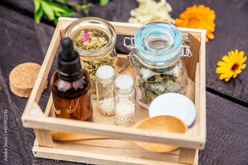 Homeopathic medicine pills on wood table, globules in jars and in wood box decorated with various herbal medicinal plants outdoors in summer, wooden background. Homeopathy concept.