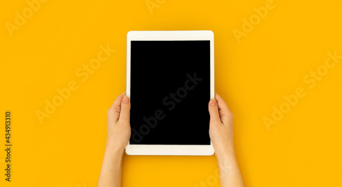 Woman hand holds digital tablet mockup with blank screen, education and application concept template, bright yellow background, top view and copy space photo