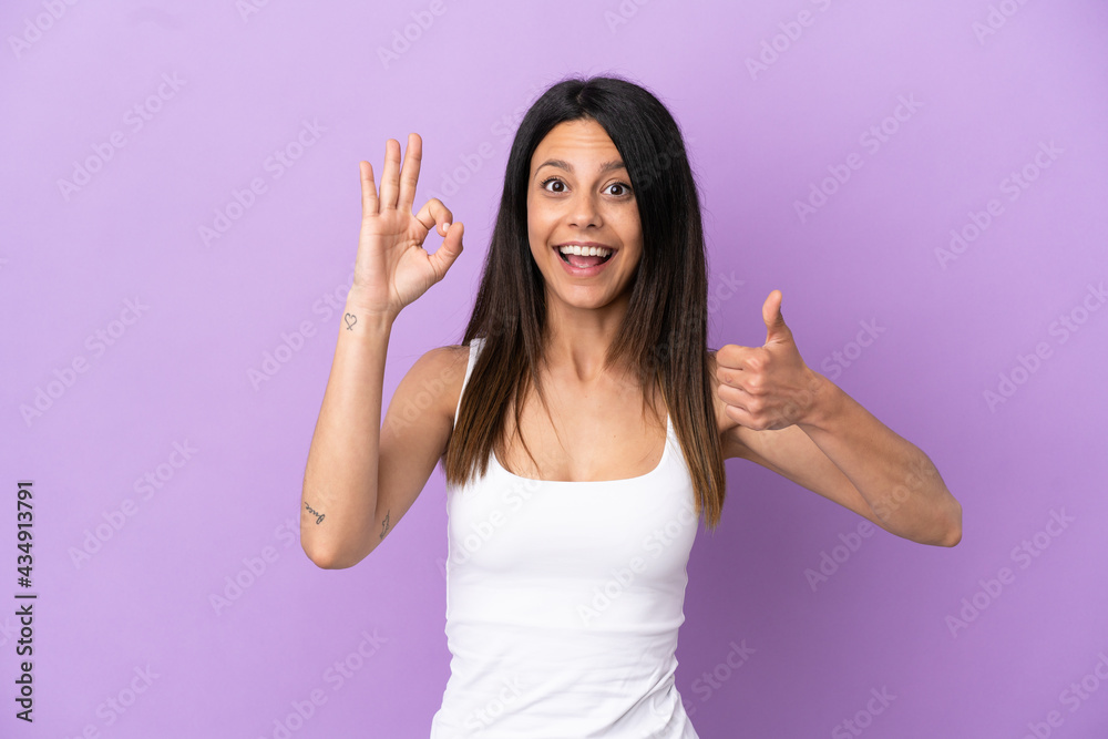Young caucasian woman isolated on purple background showing ok sign and thumb up gesture Young caucasian woman isolated on purple background showing ok sign and thumb up gesture