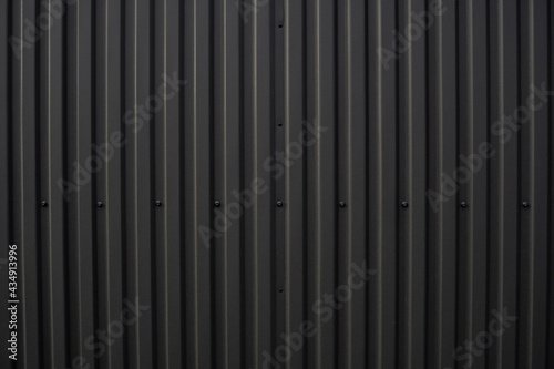 Black corrugated iron sheet used as a facade of a warehouse or factory. Texture of a seamless corrugated zinc sheet metal aluminum facade. Architecture. Metal texture.