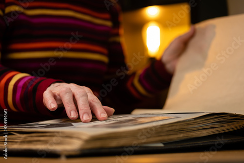 Elderly woman looks through an family album with old photos at table at home. Granny memories past times and remembering his life.