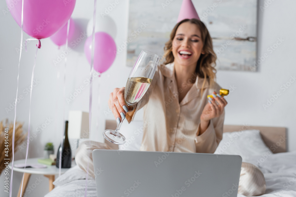 Champagne in hand of blurred woman celebrating birthday near laptop on bed