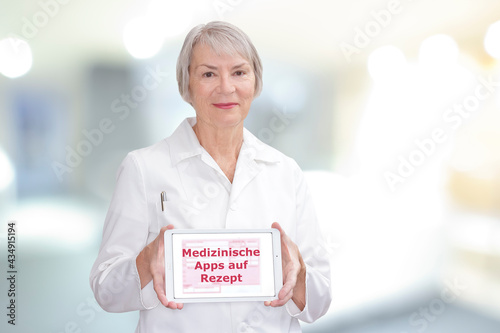 Senior doctor showing a tablet computer with the german text: Medizinische Apps auf Rezept. Translation: medicinal apps on prescription.