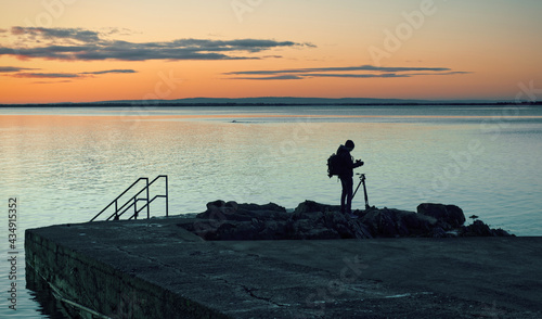 Silhouetted photographer taking shot of Blacrock tower at sunrise on Salthill beach in Galway, Ireland, lifestyle concept, nature background photo