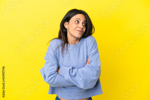 Young caucasian woman isolated on yellow background making doubts gesture while lifting the shoulders © luismolinero