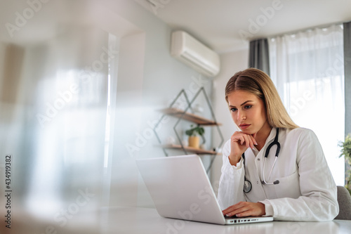 Blonde doctor, dressed in a medicine uniform, using laptop.