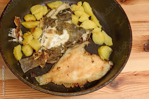 Top view of a frying pan with fried potatoes and flounder