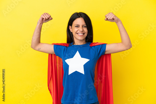 Woman isolated on yellow background in superhero costume and doing strong gesture photo
