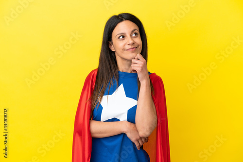 Woman isolated on yellow background in superhero costume and thinking