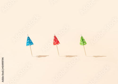 Colorful sun umbrellas with sunny day shadows against a bright beige background. Minimal summer vacation concept. Creative beach idea.