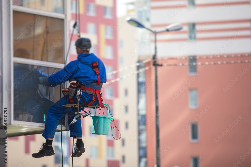 Professional climber rope access worker cleaning the windows on the high rise building, industrial mountaineers washing the glass facade of a modern building, working at heights