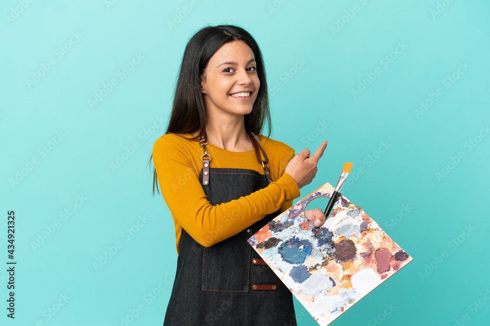Young artist caucasian woman holding a palette isolated on blue background pointing back - obrazy, fototapety, plakaty 