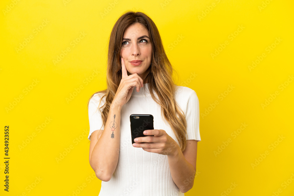 Caucasian woman isolated on yellow background using mobile phone and thinking Caucasian woman isolated on yellow background using mobile phone and thinking