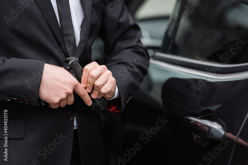 cropped view of safeguard in suit holding gun near blurred modern auto