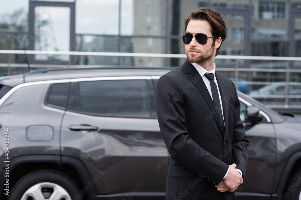 businessman in suit and sunglasses standing near modern car