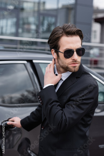 bearded safeguard in suit and sunglasses adjusting security earpiece while opening car door © LIGHTFIELD STUDIOS