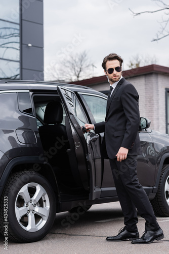 bearded bodyguard in suit and sunglasses with security earpiece opening car door © LIGHTFIELD STUDIOS