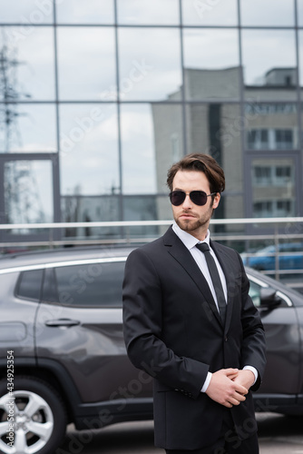 bearded safeguard in suit and sunglasses near car