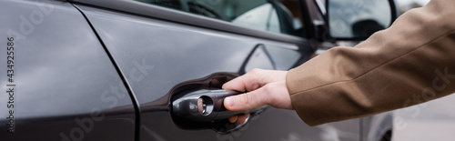 cropped view of male hand reaching door of black shiny car, banner